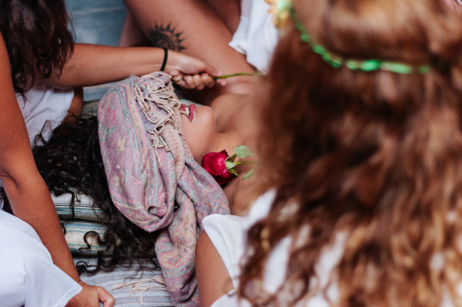 Mulher com os olhos vendados segurando uma rosa vermelha em ritual entre outras mulheres