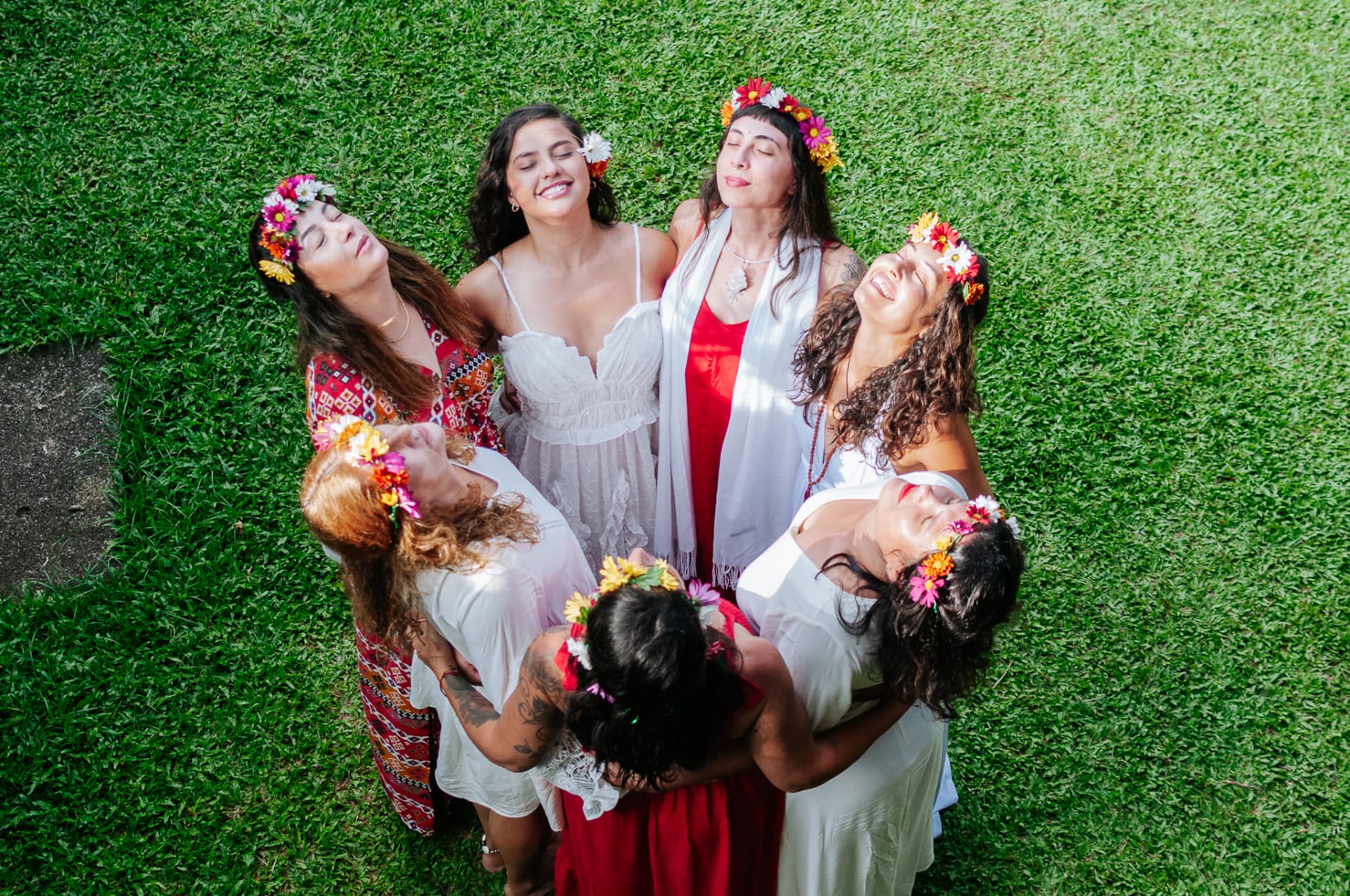 Círculo de mulheres com coroas de flores deitadas na grama, sorrindo